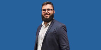 Homem com barba e óculos sorrindo.